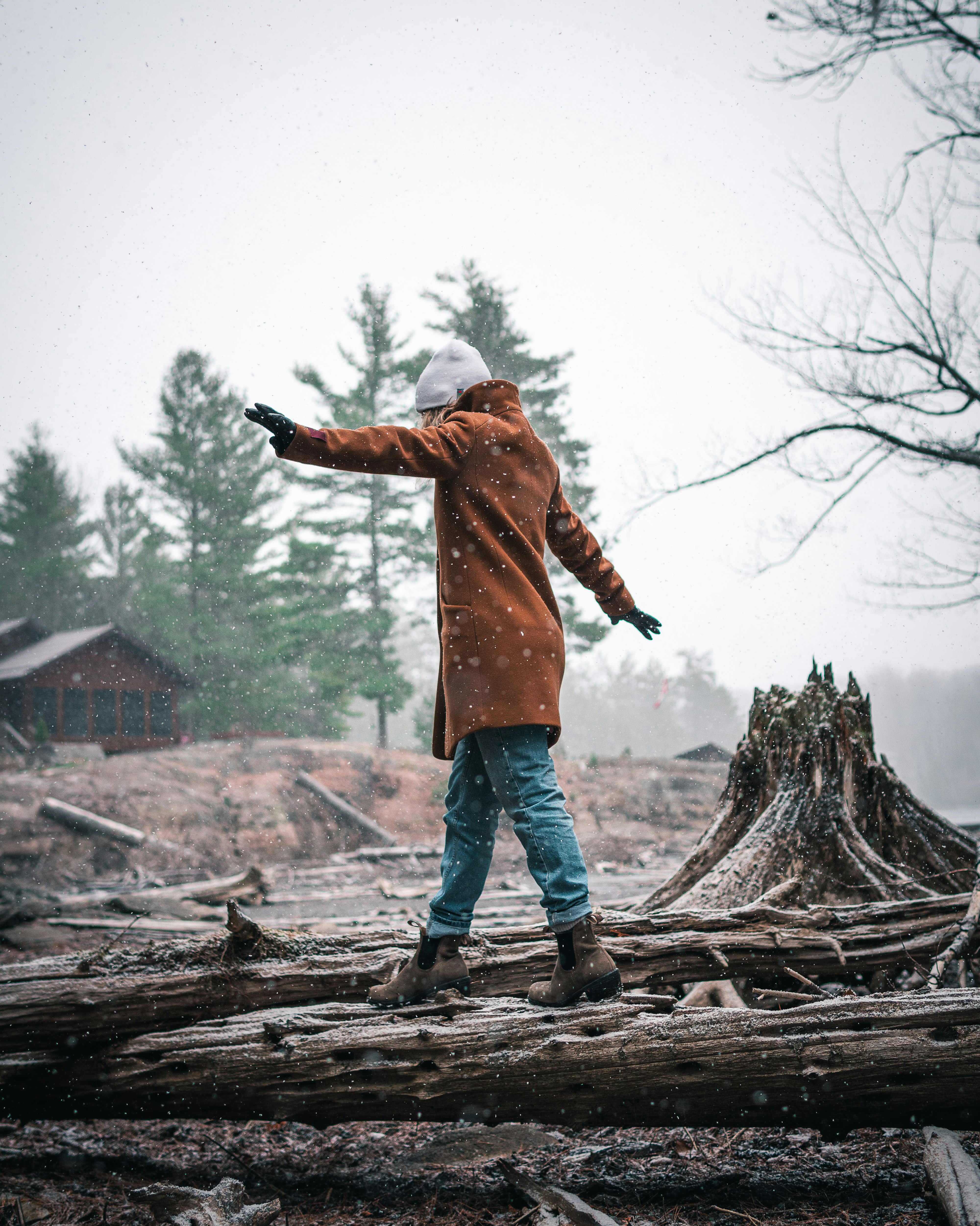 man in brown jacket and blue denim jeans standing on brown wooden log during daytime